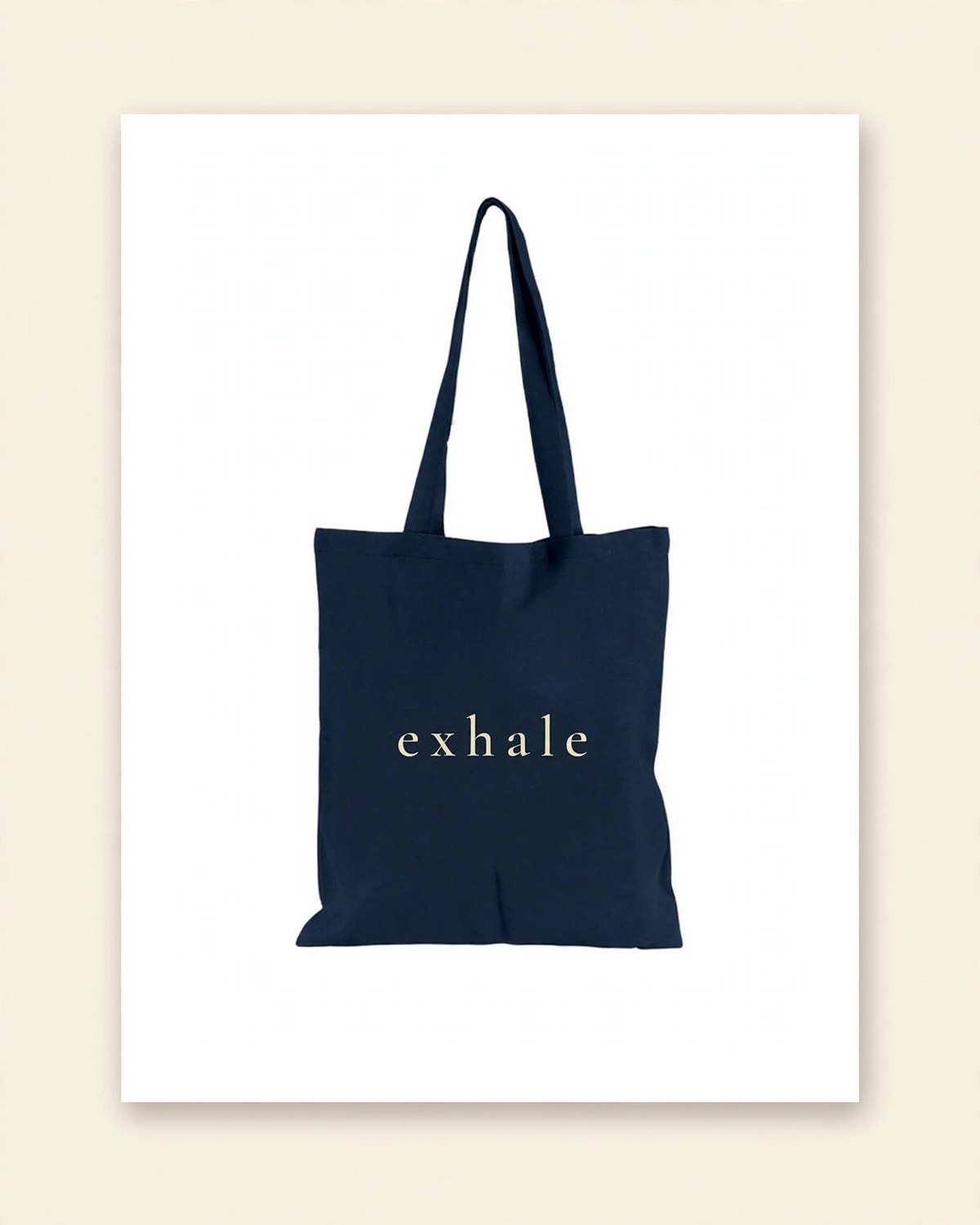 Shop mockup of the back of the Breathe Tote in navy canvas: the single word exhale in cream serif lettering, on a white card
